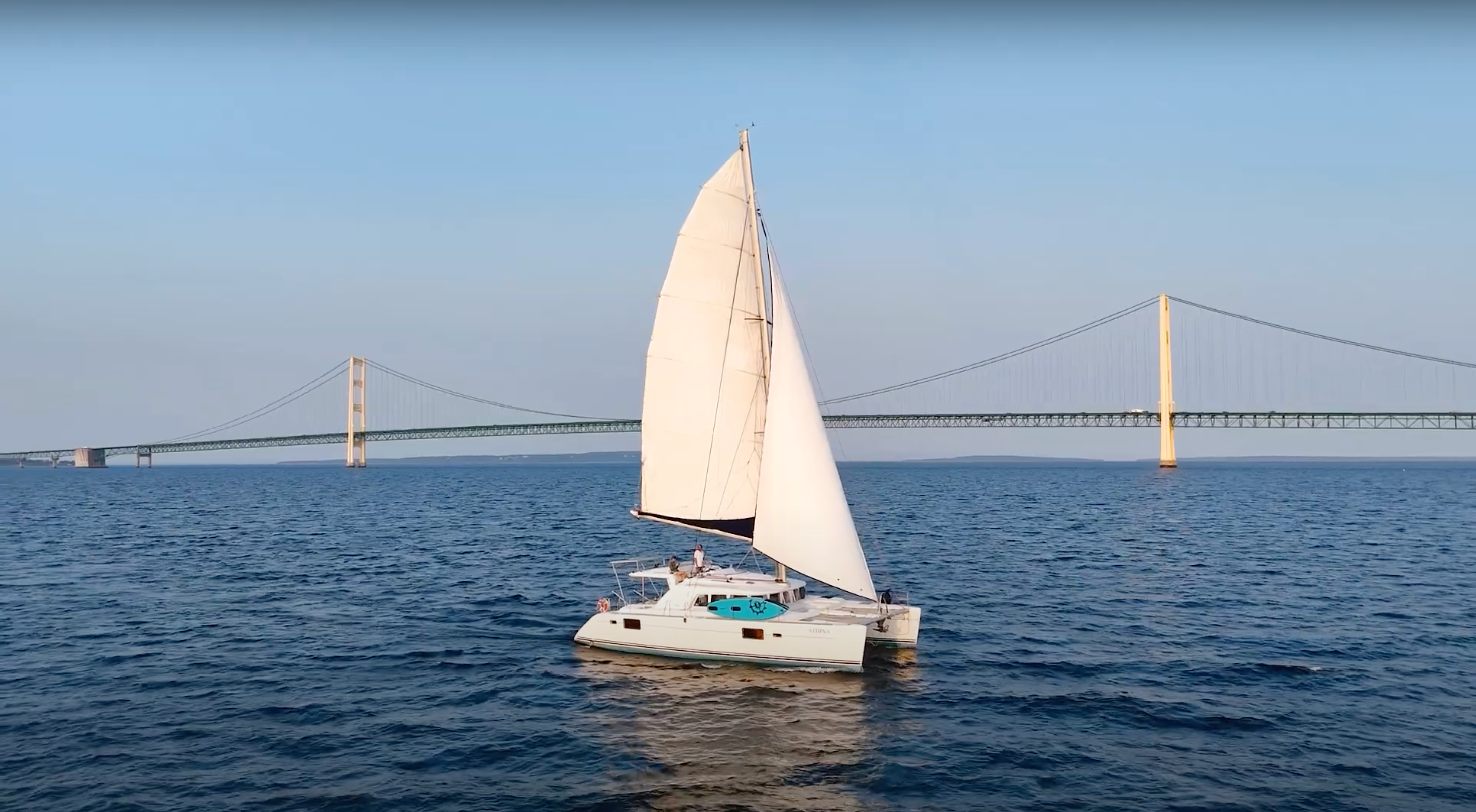 Load video: Drone video of a white catamaran in front of the Mackinac Bridge.